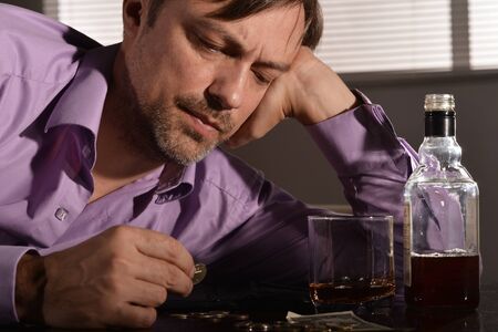 Young man sleeping with whiskey and money at table