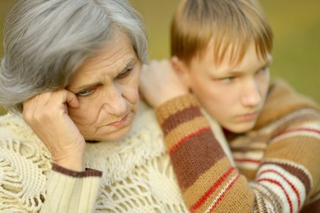 Sad Grandmother with boy in the autumn parkの写真素材