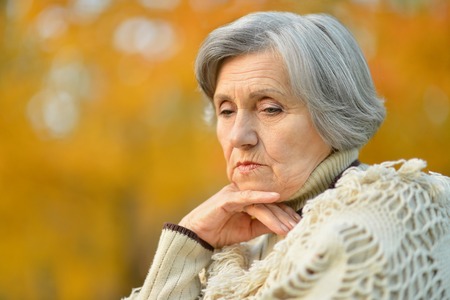 Portrait of thinking senior woman in autumn parkの写真素材