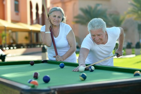 Amusing old couple on vacation playing billiards