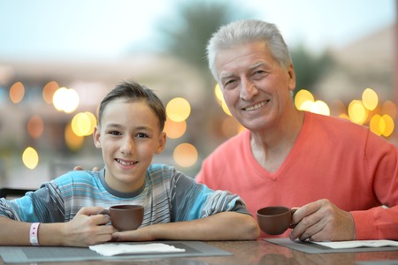 Happy boy with grandfather at breakfast with coffee on the tableの写真素材