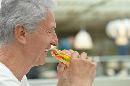 Portrait of happy elderly man eating fast foodの写真素材