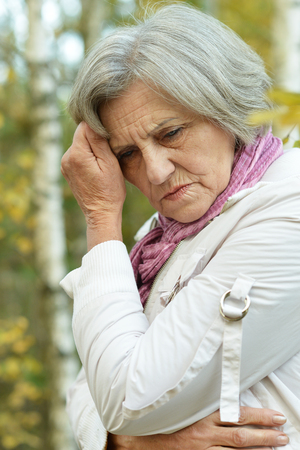 Portrait of thinking senior woman in autumn parkの写真素材