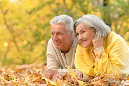 Mature couple lying on leaves in the autumn parkの写真素材