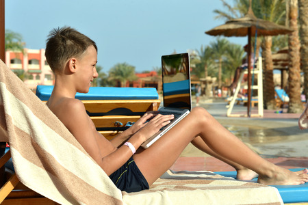 Portrait of a happy boy with laptop near poolの写真素材