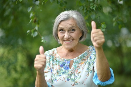 Senior woman showing thumbs up in the parkの写真素材