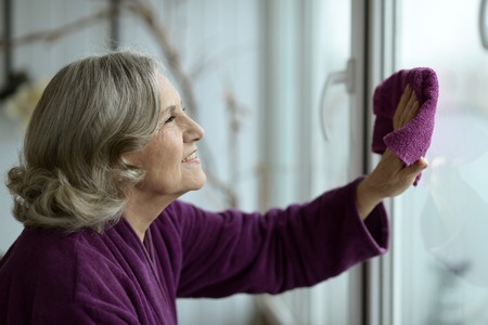 Portrait of a senior woman cleaning window at homeの写真素材