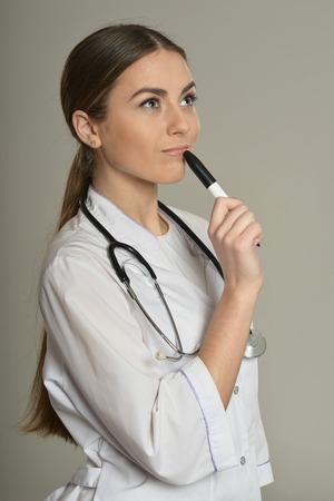 Female doctor standing with a felt pen on grey backgroundの写真素材