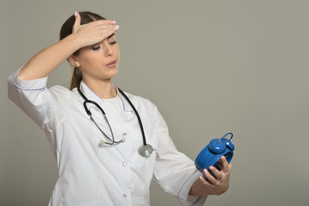 Female doctor with clock, standing on grey backgroundの写真素材