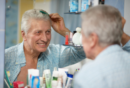 Senior man combing hair in the bathroomの写真素材