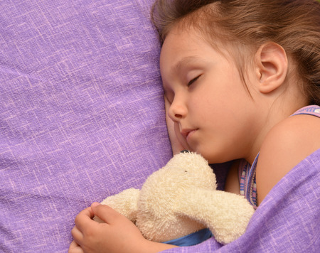 Cute little girl sleeping with a toy in her bedの写真素材
