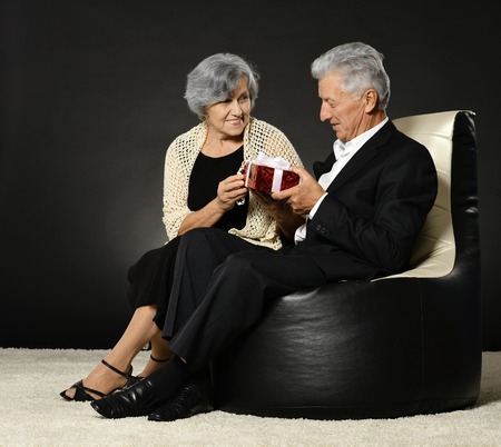 Senior couple sitting in armchair and celebrating holiday with giftの写真素材