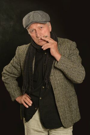 Senior man smoking cigarette over black background