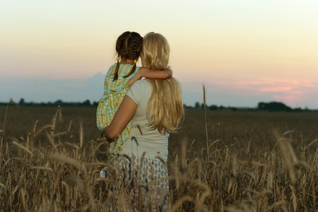 Young mother and her daughter at the wheat field on sunset,back viewの写真素材