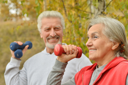 Happy fit senior couple exercising with dumbbells in autumn parkの写真素材
