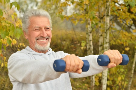Elderly man exercising with dumbbells in autumn parkの写真素材