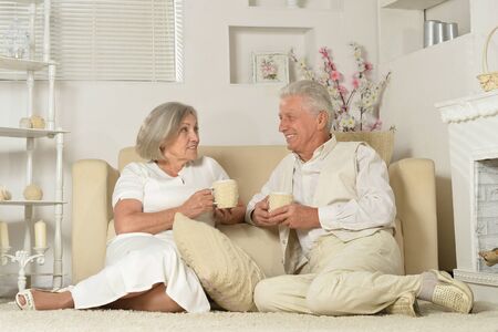 Two elderly people sitting near couch with tea