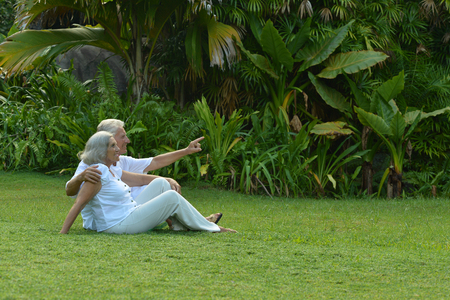 Happy elderly couple  sitting on grass  in tropical garden outdoorの写真素材