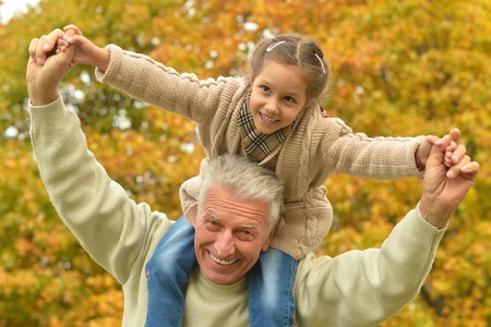 Happy elderly man with granddaughter in autumn parkの写真素材
