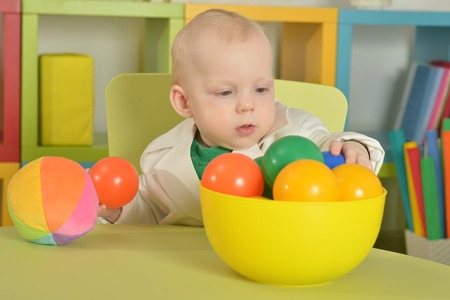 cute little boy sitting on chair with toys in roomの写真素材