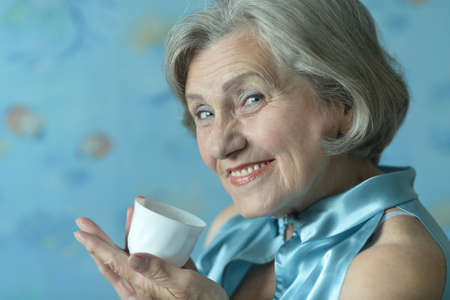 Portrait of happy retired woman drinking tea on blue backgroundの写真素材