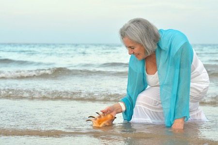 Happy senior woman with shell on beachの写真素材