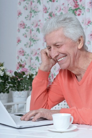 Portrait of  senior man  in the kitchen at home with laptop