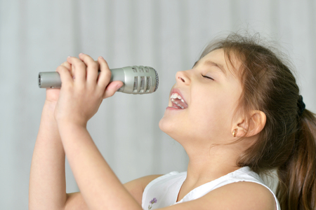 Beautiful little girl with microphone at homeの写真素材
