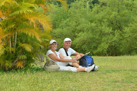 Beautiful happy elderly couple rest at tropical resort with backpacks and mapの写真素材