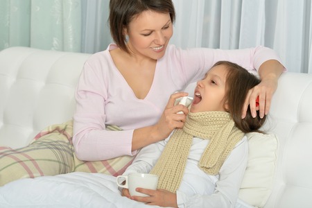 Sick little girl with mother in bed with hot drink at homeの写真素材