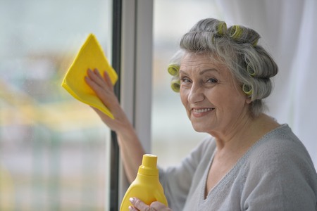 Portrait of a senior woman cleaning window at homeの写真素材