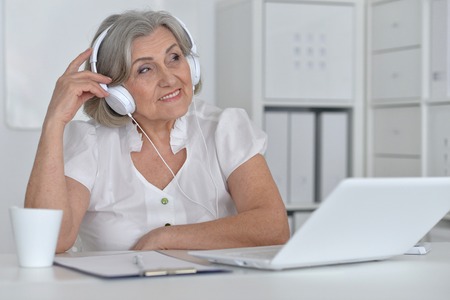 Portrait of a senior woman with headphones and laptopの写真素材