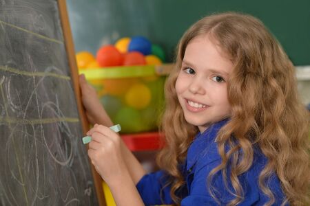 Pretty little girl writing on chalkboard at school