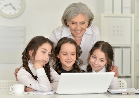 Three beautiful little girls and old woman using a laptopの写真素材