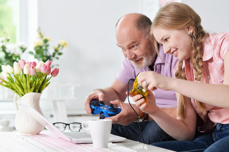 portrait of happy grandfather and little granddaughter playing video games