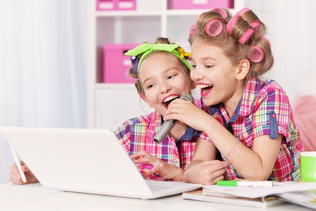 Cute  tweenie girls  in hair curlers  with laptop ,singing in karaoke at homeの写真素材