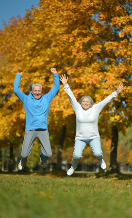 Happy fit senior couple jumping in autumn parkの写真素材