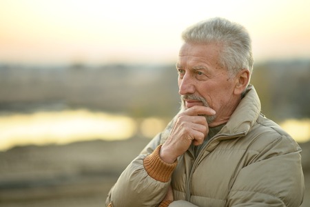 close-up portrait of a senior man thinking about something standing outdoorsの写真素材