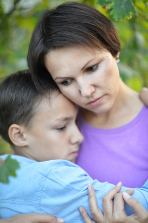 Portrait if young mother and her preteen son hugging, looking serious