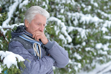 Portrait of thoughtful senior man in a snow-covered winter parkの写真素材