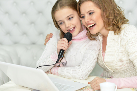 Young mother and her cute daughter singing karaoke at homeの写真素材