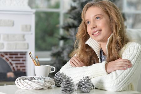 Portrait of happy teen girl with Christmas decorations sitting at the table at homeの写真素材