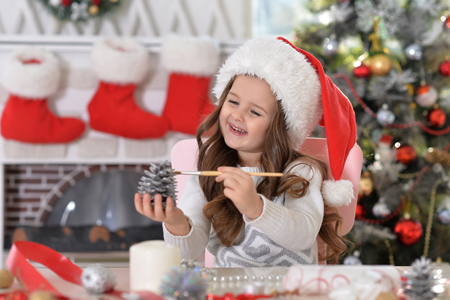 Portrait of happy little girl in Santa hat with pine cone decorationの写真素材