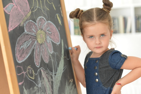 cute little girl posing near blackboard, with drawing flowers