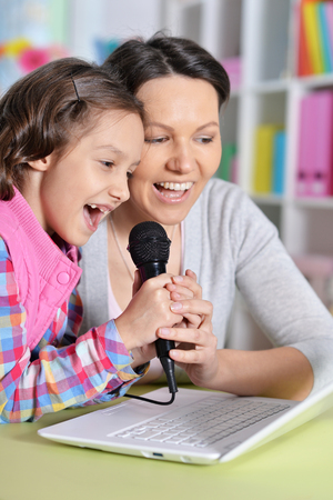 girl sitting at table and singing karaoke with motherの写真素材