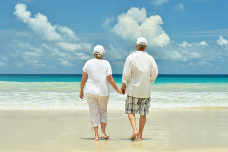 Happy elderly couple resting on sandy beach near tropical resortの写真素材