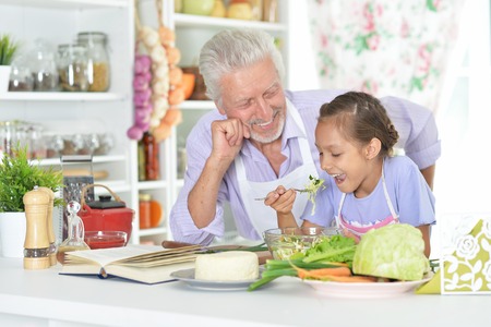 Senior man with granddaughter preparing dinner in kitchenの写真素材