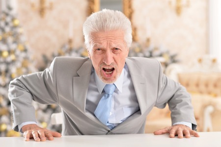 Close up portrait of angry senior businessman sitting at tableの写真素材