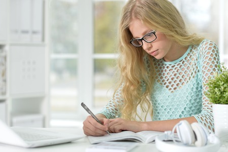 Portrait of middle aged woman with daughter hugging at homegirl with eyeglasses on sitting at desk and studyingの写真素材