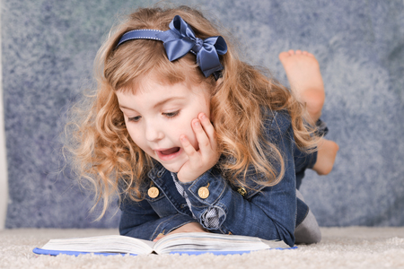 Portrait of cute little girl reading book while lying on floorの写真素材